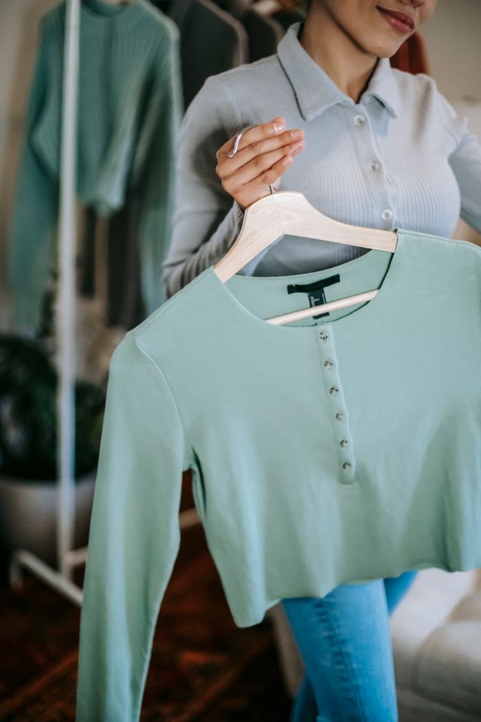 Home Crop anonymous woman in blouse and jeans at home near wardrobe with blue cloth on hanger