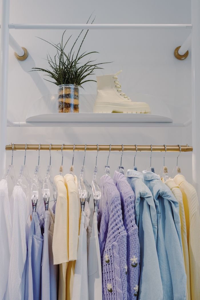 Home A stylish display of pastel clothes on hangers in a modern boutique with fashion boots and a decorative plant.